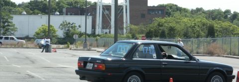 2001 Mercury Grand Marquis - A black BMW E30 coupe is parked in a lot, with orange cones and other vehicles in the background.