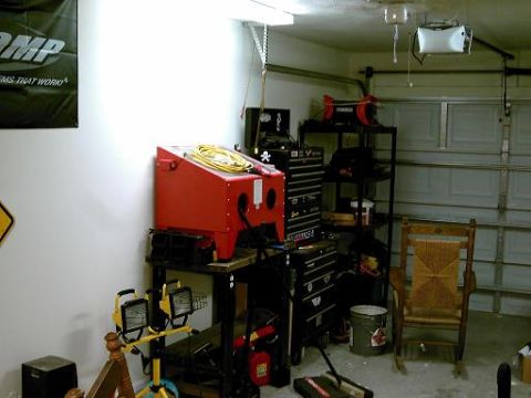 1986 Ford Bronco - A cluttered garage scene displays various tools and equipment, including a red sandblaster and multiple tool chests.