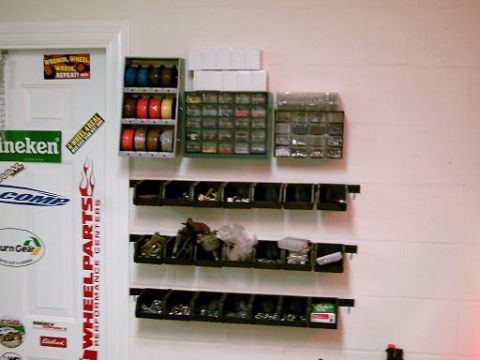 1986 Ford Bronco - A door covered in stickers is next to a wall with shelves holding various parts bins and organizers.