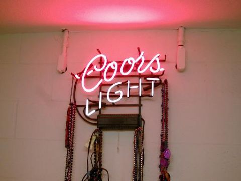 1986 Ford Bronco - A Coors Light neon sign hangs above beaded necklaces against a white wall.