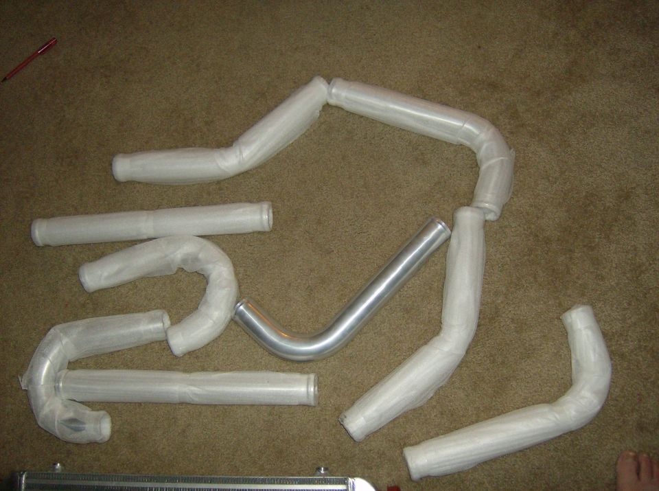 Aluminum radiator hoses, some wrapped in plastic, laid out on carpet
