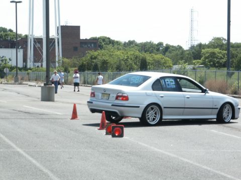 2001 Mercury Grand Marquis - Silver BMW E39 sedan with racing numbers on windows navigates an autocross course marked by orange cones.