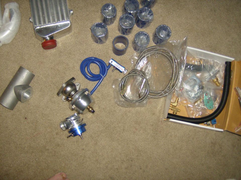 Car parts laid out on carpet: intercooler, blow-off valve, piping, and hoses