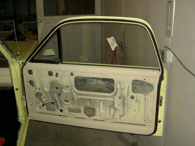 Interior of a car door, showing the bare metal frame and window mechanism. A piece of paper is taped to the inside of the window
