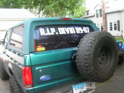 1996 Ford Bronco - Teal 1996 Ford Bronco rear view shows spare tire and memorial decal; blue Jeep in background.