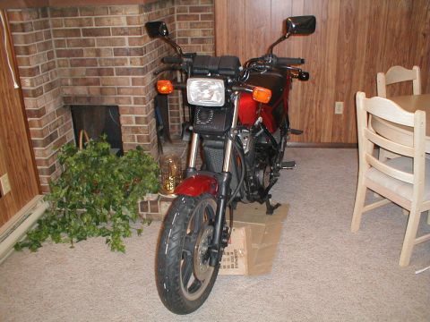 1991 Ford Bronco - A red motorcycle is positioned indoors in front of a brick fireplace, with a dining set visible in the background.