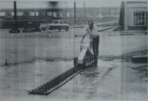 2000 Ford E350 - A man operates a tracked machine on a ramp, with a pickup truck visible in the background.