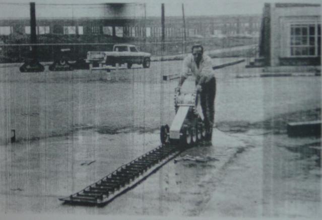 Man operating a tracked machine on a ramp with a pickup truck in the background