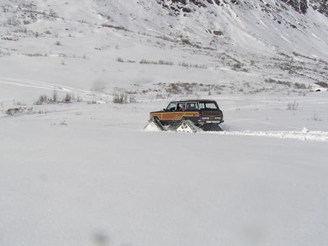 2000 Ford E350 - A wood-paneled SUV equipped with snow tracks navigates a snow-covered terrain with a mountain in the background.