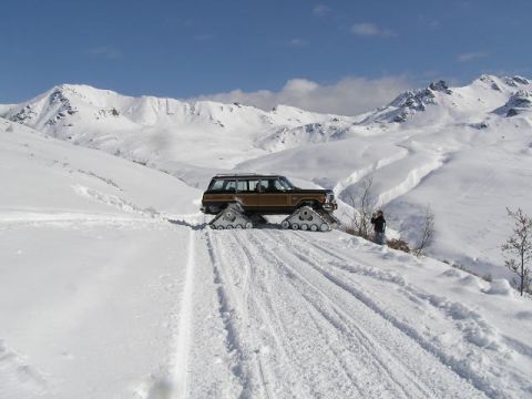 2000 Ford E350 - A van modified with snow tracks navigates a snow-covered mountain path under a clear blue sky.