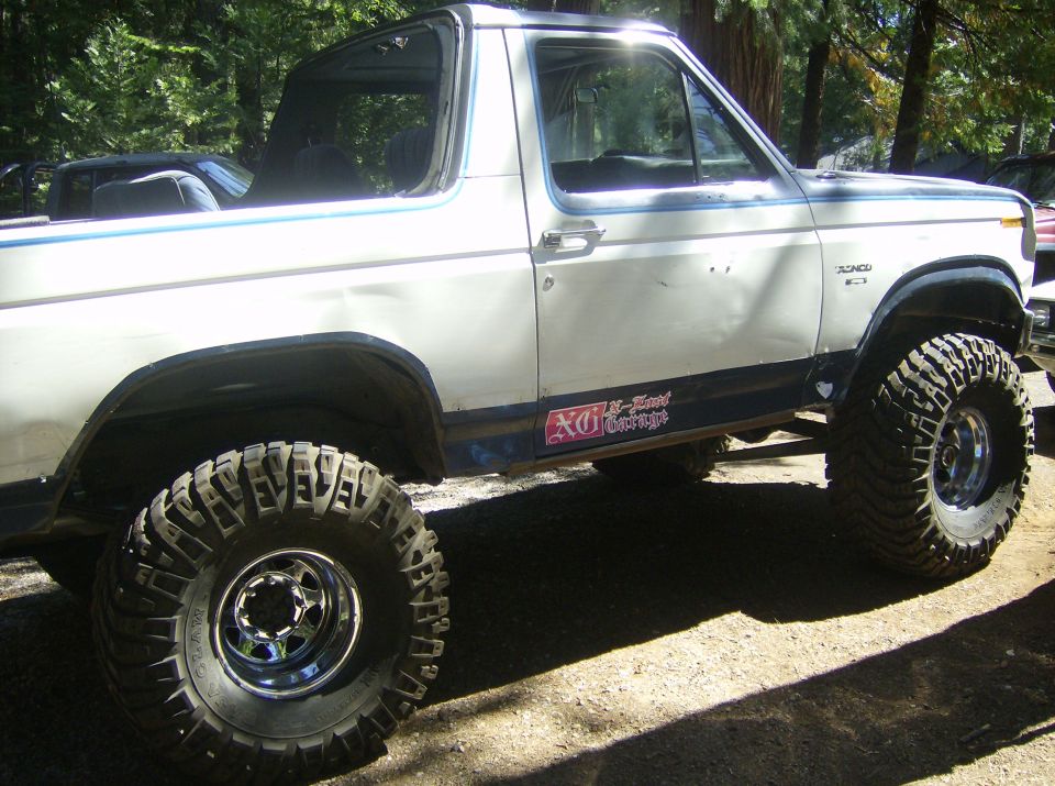 White 1986 Ford Bronco with custom wheels and large off-road tires parked outdoors. Decal on door reads 'X-Treme Garage'