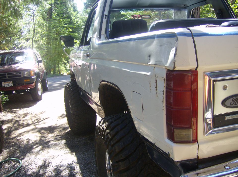 White Ford Bronco with large tires, parked next to a red Toyota SUV