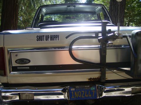 1986 Ford Bronco - Rear view of a white Ford Bronco with a "SHUT UP HIPPY" sticker and a bike rack attached.