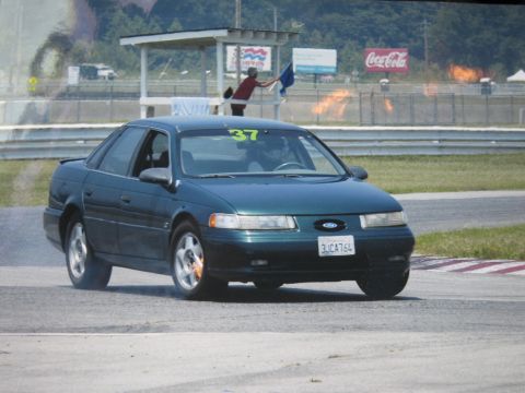 1997 Ford Taurus - A dark green 1997 Ford Taurus with racing number 37 on the windshield navigates a turn on a race track.