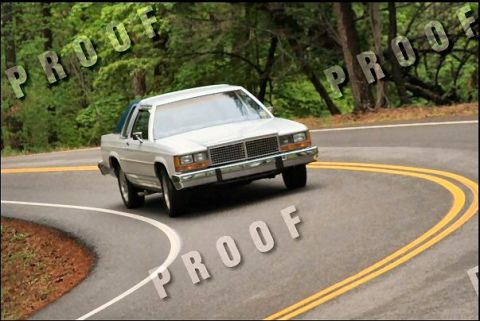 1985 Ford LTD Crown Victoria - A white sedan navigates a curve on a tree-lined road.