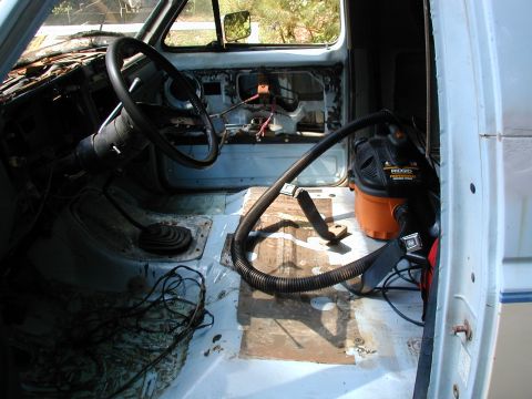 1986 Ford Bronco - The interior of a 1986 Ford Bronco is shown with the floor stripped and a shop vac present, indicating cleaning or restoration work.