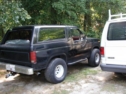 1986 Ford Bronco - A black Ford Bronco is parked next to a white van in an outdoor setting.