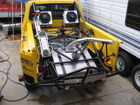 1984 Ford Bronco - Modified yellow truck with custom rear suspension and fuel system, viewed from the back.