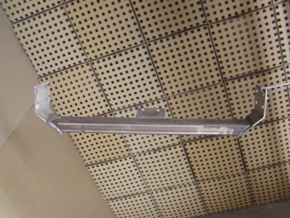 Metal crossmember with bracket attached, mounted against a perforated panel