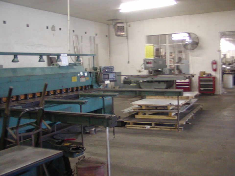 Workshop with large metal cutting machine, grinder, and stacked metal sheets
