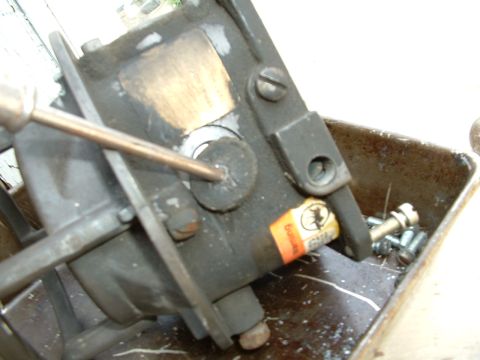 1978 Ford Bronco - Carburetor part with a screwdriver inserted, showing an orange label with text and a bin of screws.