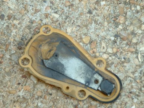 1978 Ford Bronco - A close-up view of an automotive part with a yellow gasket and metal components, resting on a gravel surface.