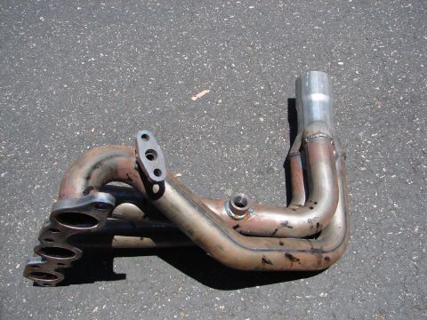 1992 Ford Taurus - An exhaust manifold part is shown on asphalt, with visible weld marks and signs of wear.