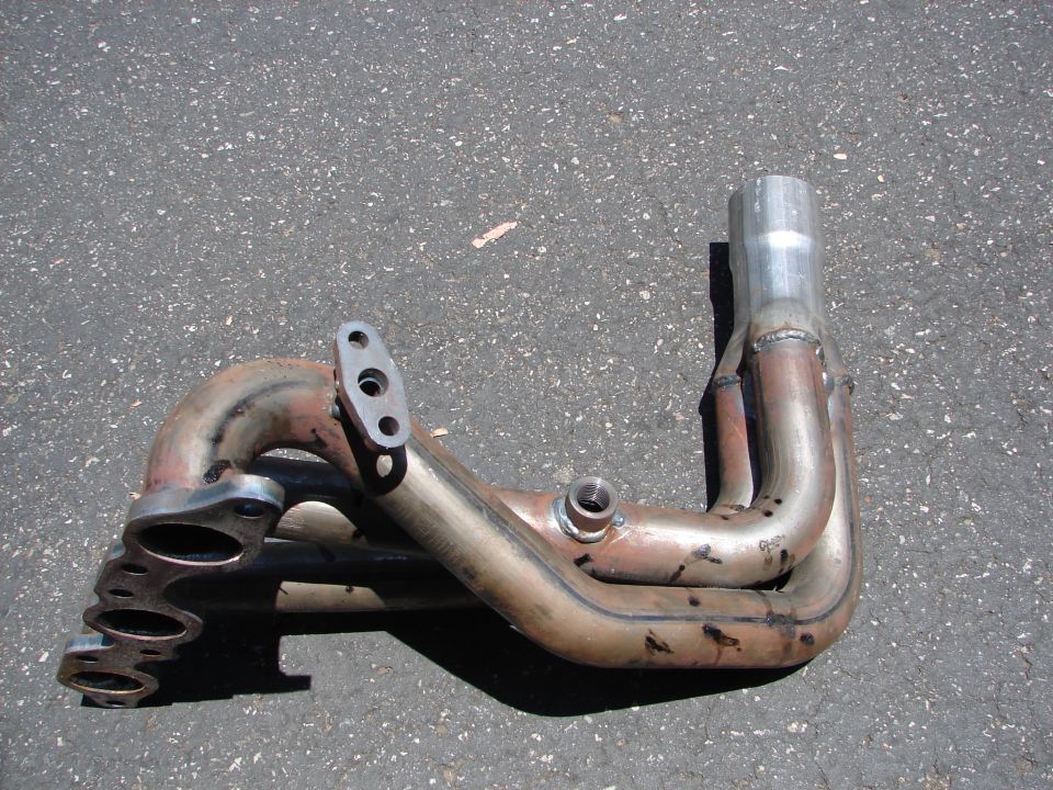 Exhaust manifold with four pipes merging into one, made of metal with rust and weld marks