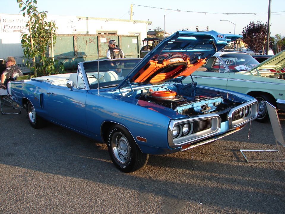 Blue 1970 Dodge Super Bee convertible with hood open, showing engine. Another classic car is parked next to it