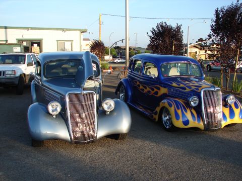 1992 Ford Taurus - A silver hot rod with its hood up sits next to a blue hot rod adorned with flame graphics.