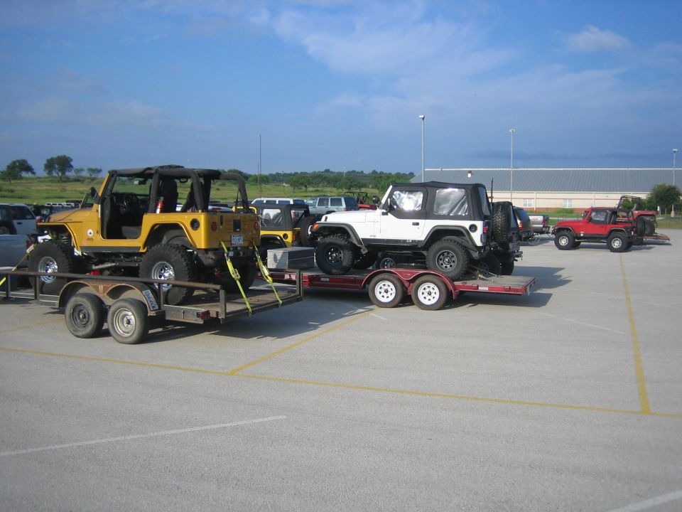 Yellow Jeep Wrangler on trailer, white Jeep Wrangler on trailer, red Jeep Wrangler parked nearby