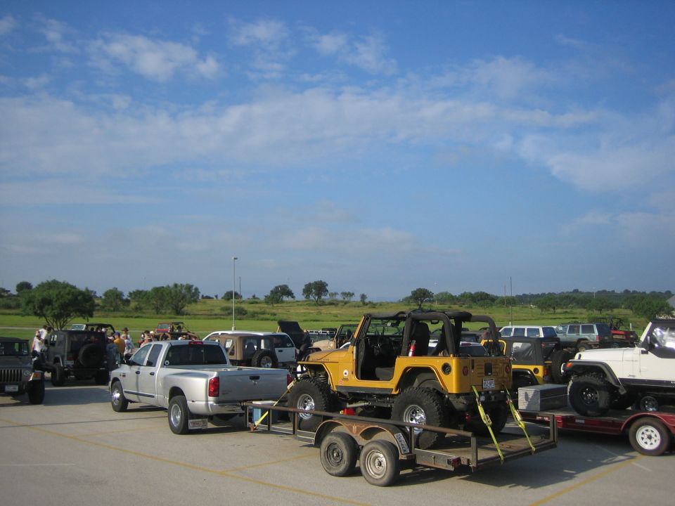 Yellow Jeep Wrangler on trailer, silver pickup truck, other Jeeps and SUVs in background