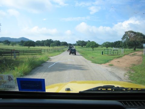 2001 Jeep Wrangler - A convoy of Jeeps travels down a dusty road through a rural landscape under a partly cloudy sky.