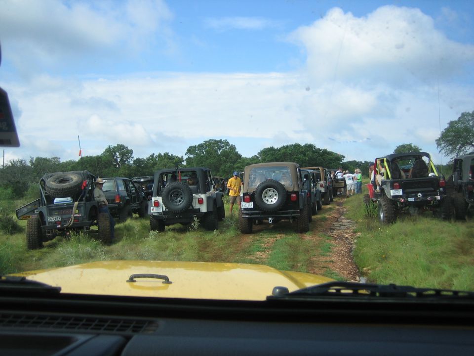 Several Jeeps lined up on a dirt path with trees and cloudy sky