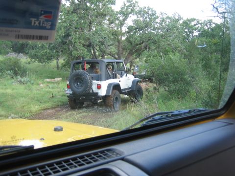 2001 Jeep Wrangler - A white 2001 Jeep Wrangler is seen from another vehicle's interior, driving on a dirt path surrounded by trees.