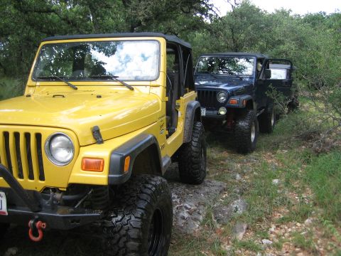2001 Jeep Wrangler - Two Jeep Wranglers are parked on a muddy, rocky trail surrounded by trees and brush.