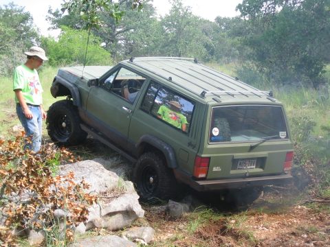 2001 Jeep Wrangler - A green Jeep Cherokee XJ navigates rocky terrain with a person standing nearby.