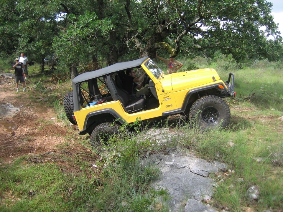 Yellow 2001 Jeep Wrangler TJ with soft top on a rocky trail, front passenger side visible