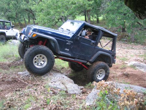 2001 Jeep Wrangler - A blue Jeep Wrangler navigates a rocky off-road trail, with a white Jeep visible in the background.