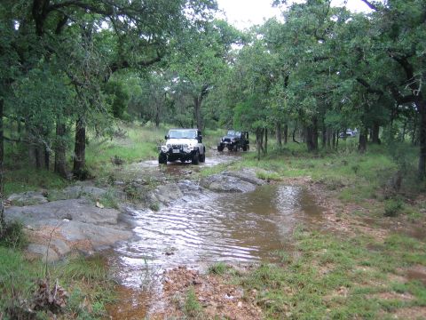 2001 Jeep Wrangler - A white 2001 Jeep Wrangler navigates a water crossing on a wooded trail, with another Jeep following behind.