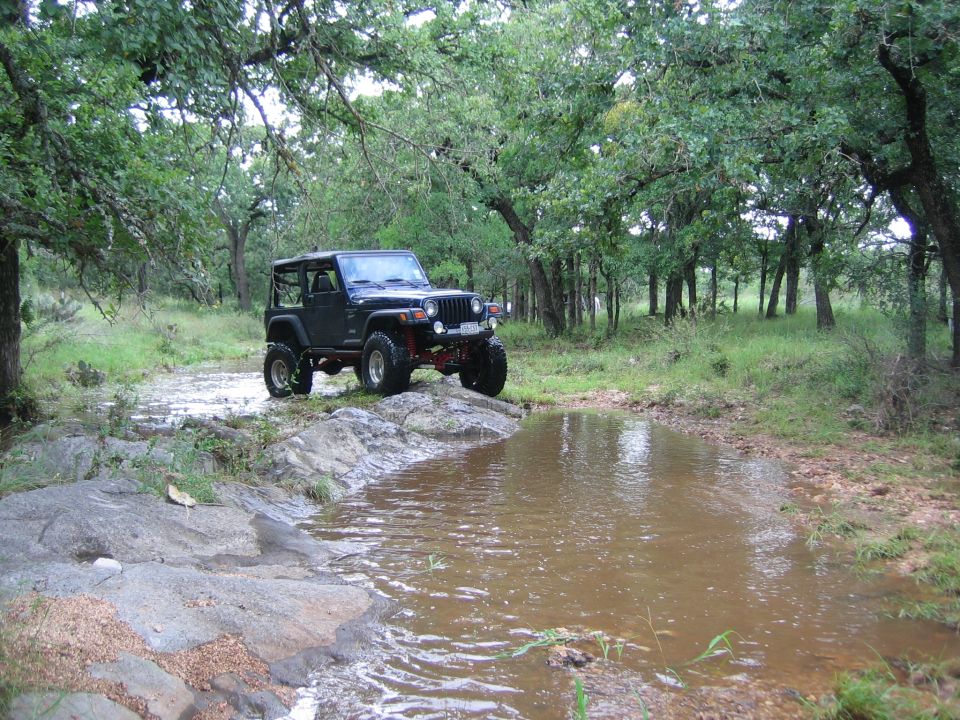 Black Jeep Wrangler on rocky terrain near water, 3/4 front view