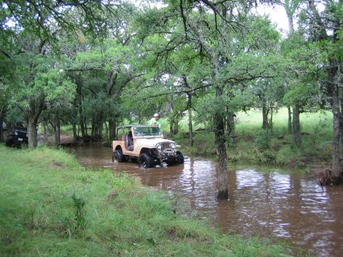 2001 Jeep Wrangler - Two Jeeps navigate a muddy stream surrounded by trees and lush green grass.