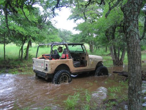 2001 Jeep Wrangler - A tan Jeep Wrangler navigates through a shallow body of water surrounded by trees.