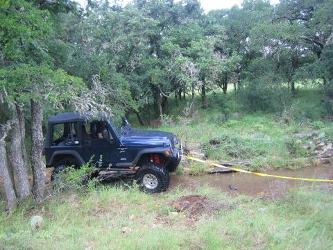 2001 Jeep Wrangler - A Jeep Wrangler navigates a water obstacle on a trail, with a tow strap attached.