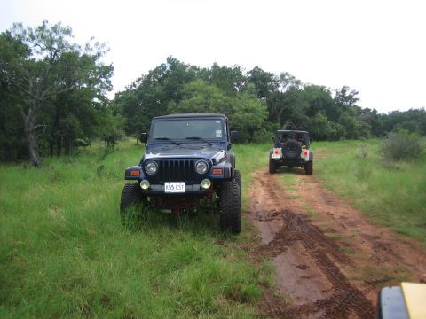 2001 Jeep Wrangler - Two Jeep Wranglers drive down a muddy dirt road through a grassy, wooded area.