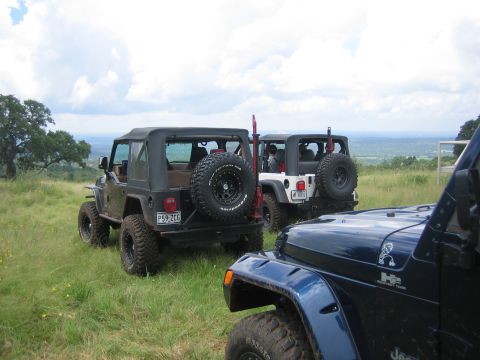 2001 Jeep Wrangler - Three Jeep Wranglers are parked on a grassy hill with a scenic view in the background.