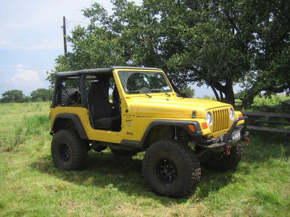 Yellow Jeep Wrangler with black soft top and off-road tires parked on grass
