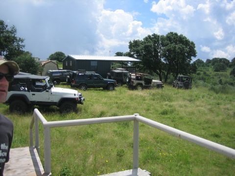 2001 Jeep Wrangler - A group of Jeeps are gathered in a grassy area with a building and trees visible.