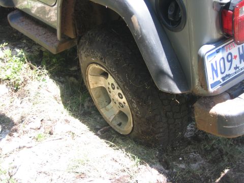 2001 Jeep Wrangler - The rear tire of a Jeep Wrangler is shown on a muddy surface, with a Texas license plate visible.