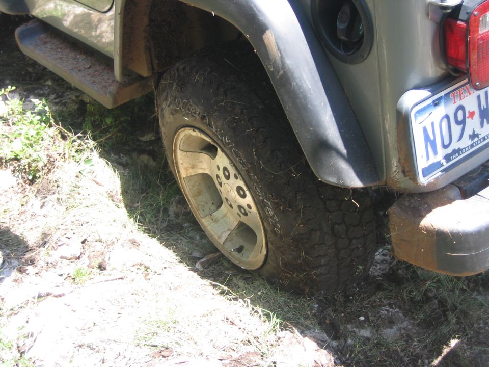 Rear tire and bumper of a 2001 Jeep Wrangler on muddy ground